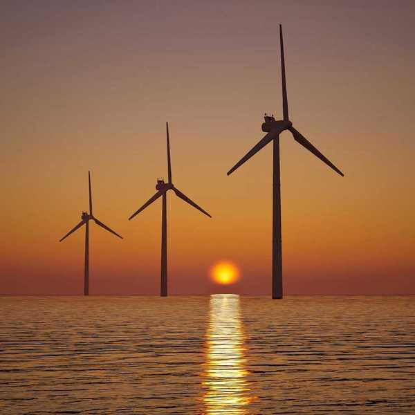 3 offshore wind turbines sillouetted against a setting (or rising) sun