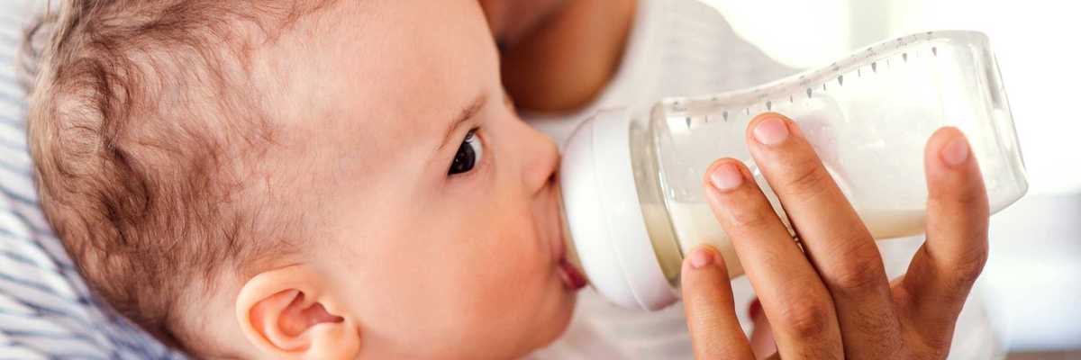 A baby drinks from a plastic baby bottle