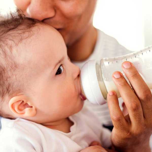 A baby drinks from a plastic baby bottle