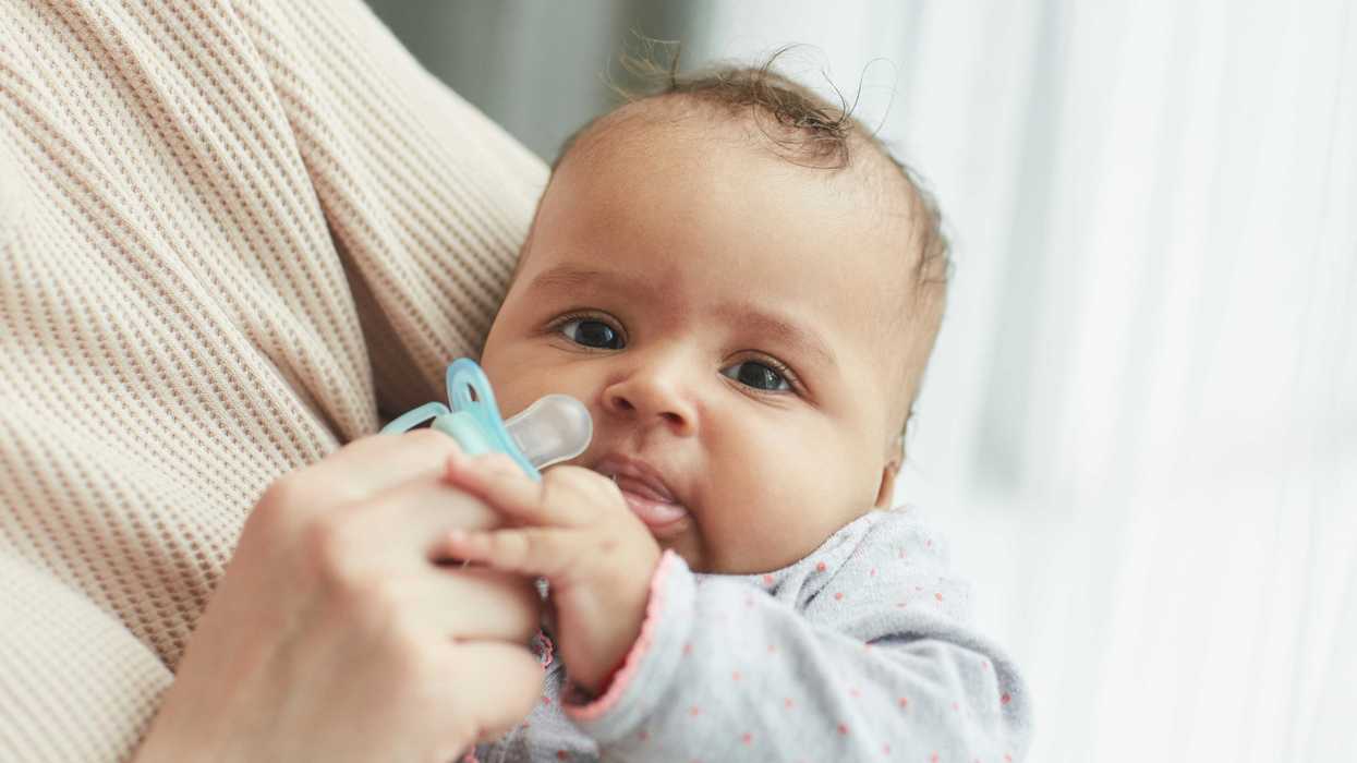 A baby hols a blue pacifier