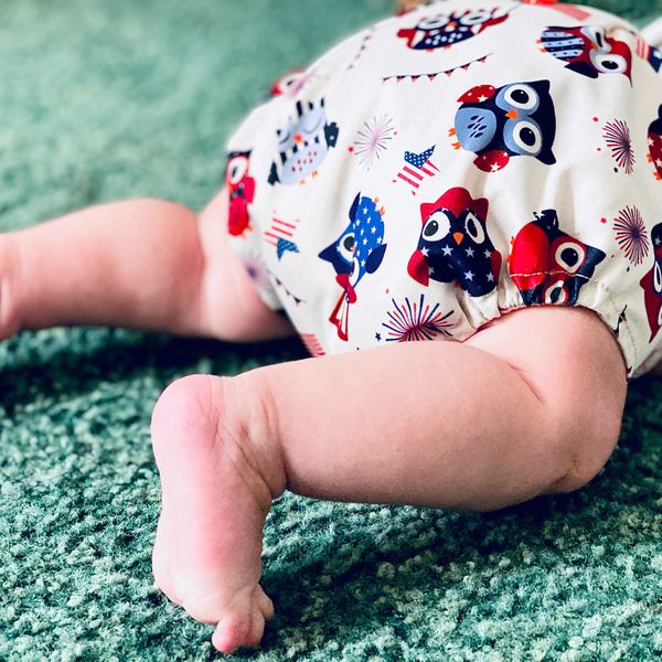 A baby's bottom half in colorful diaper crawling on a green carpet.
