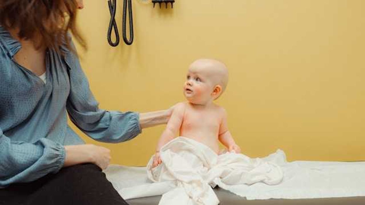A baby sitting on an exam table with its mother in a doctor's office
