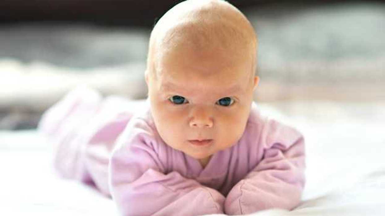 A baby wearing a pink snuggie staring intently into the camera