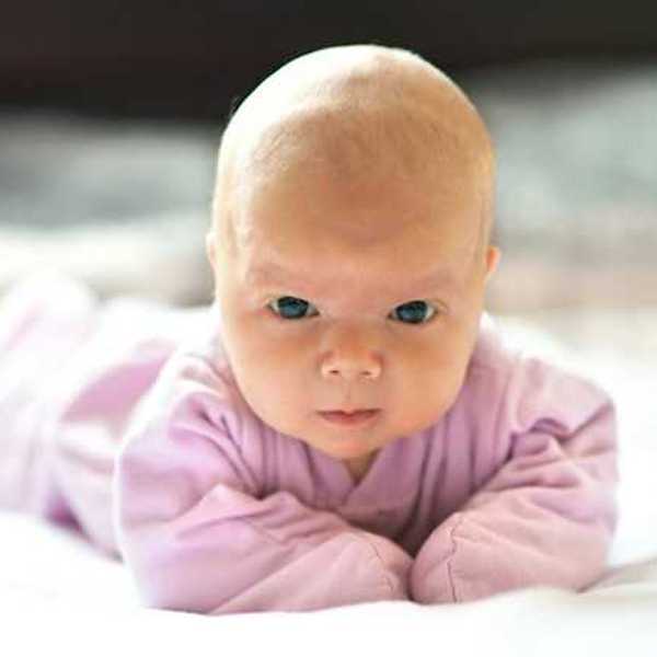 A baby wearing a pink snuggie staring intently into the camera