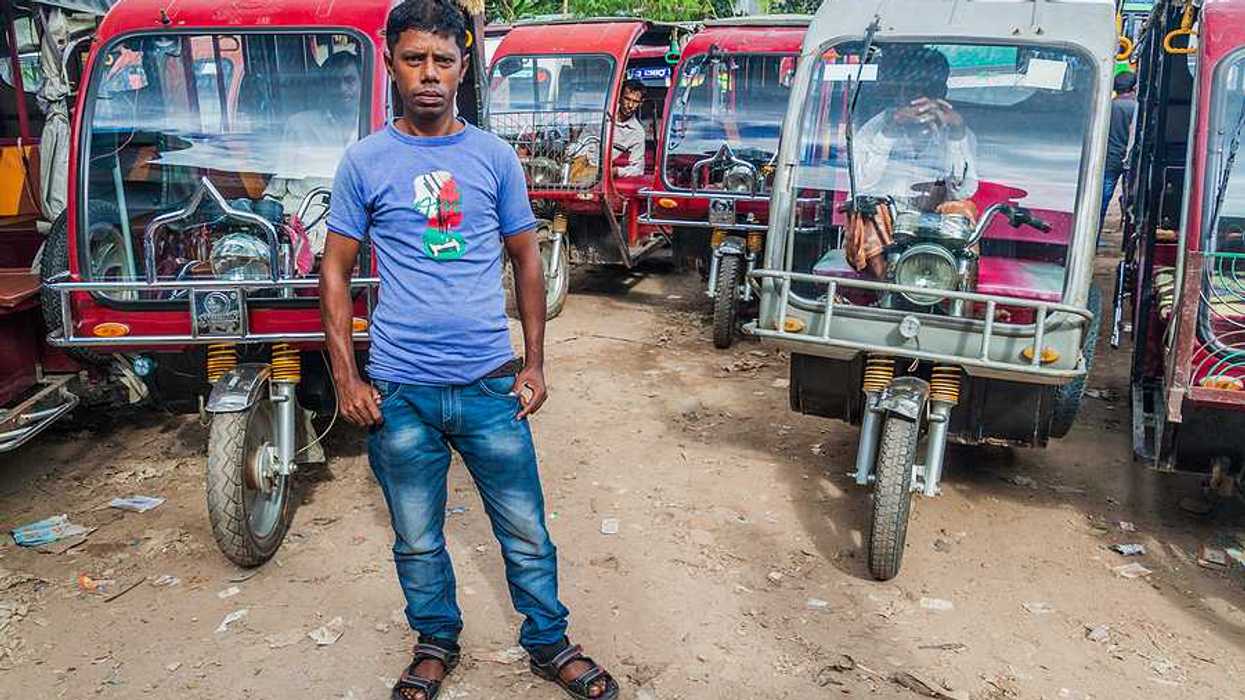 A Bangladeshi man standing in front of a group of motorcycle-powered rickshaws