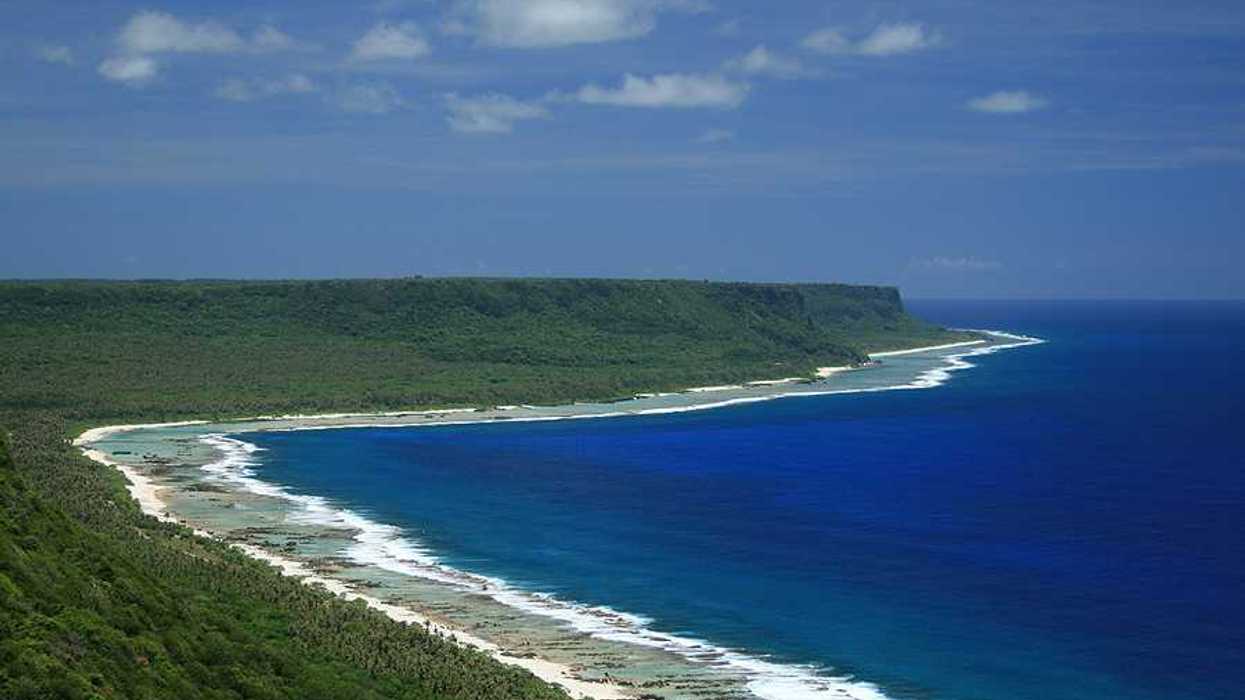 A beach alongside blue water and green hills
