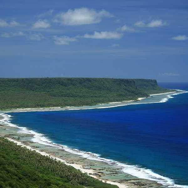 A beach alongside blue water and green hills