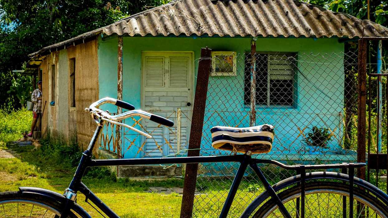 a bicycle parked in front of a small turquoise house.