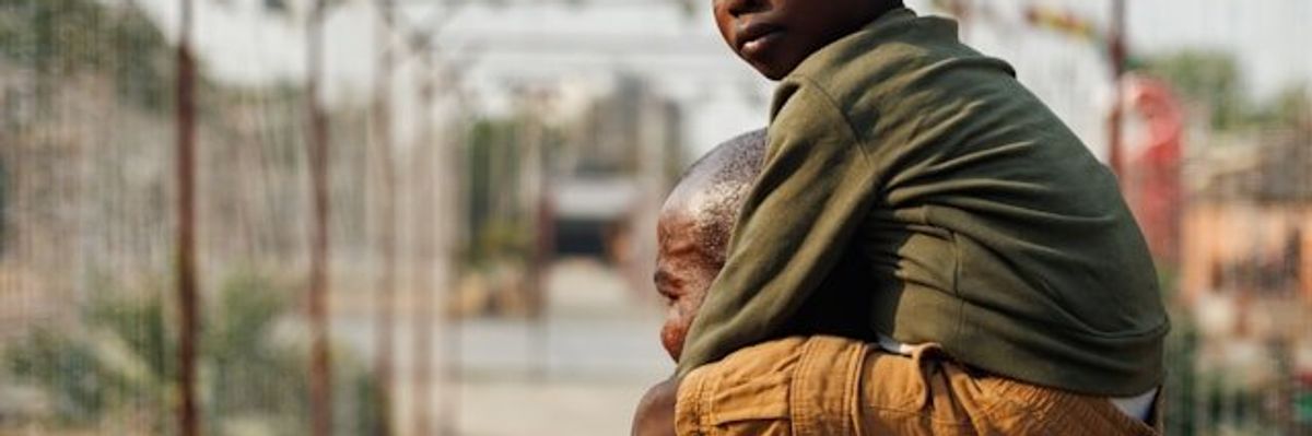 A black child looking at the camera being carried on a man's shoulders.