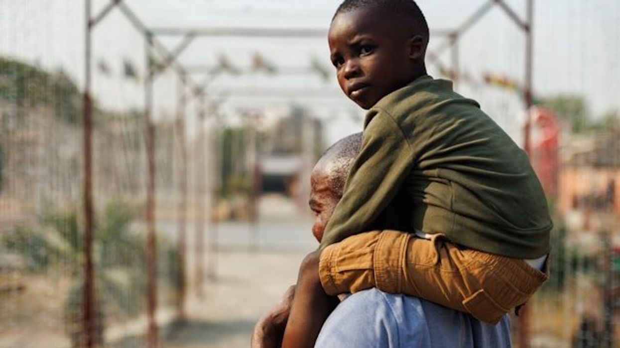 A black child looking at the camera being carried on a man's shoulders.