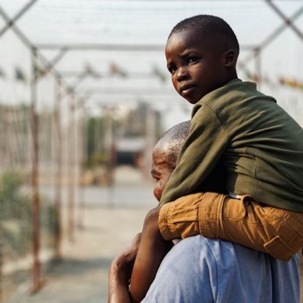 A black child looking at the camera being carried on a man's shoulders.