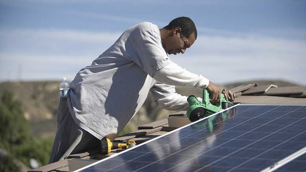 A black man installing solar panels on a roof on a sunny day