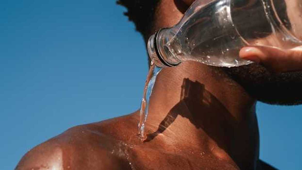 A Black man pouring a bottle of water on his shoulder on a hot day