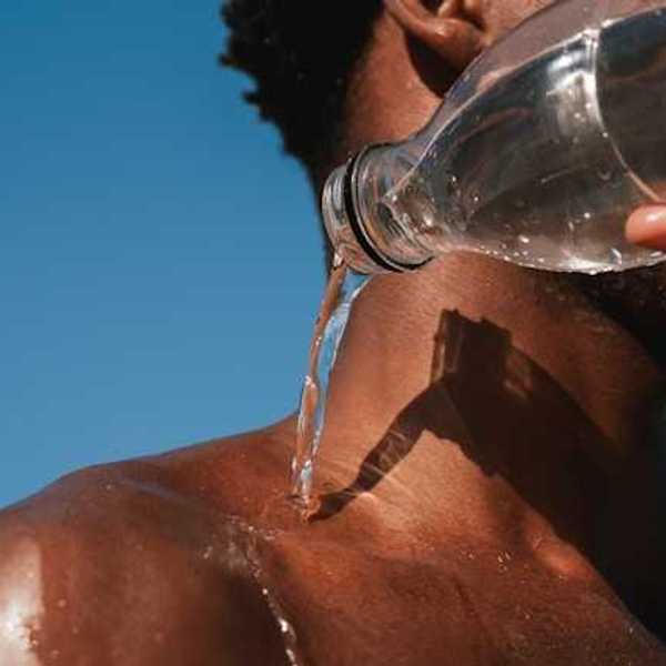 A Black man pouring a bottle of water on his shoulder on a hot day