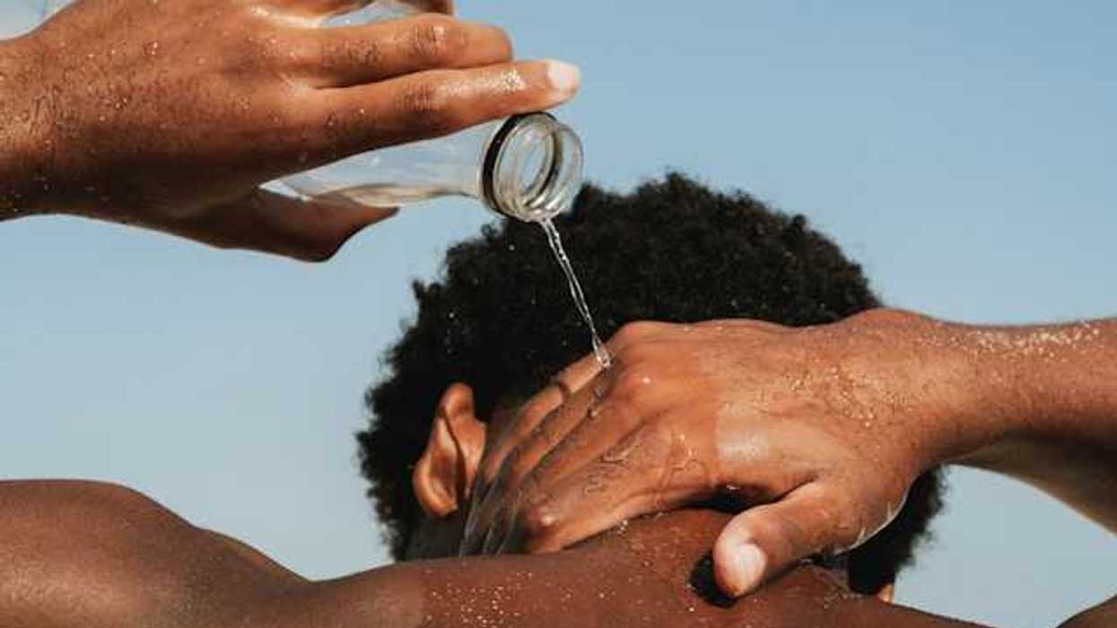 A Black man pouring water on his neck on a hot day