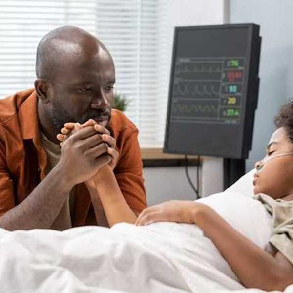 A Black man sitting at the hospital bedside of his son