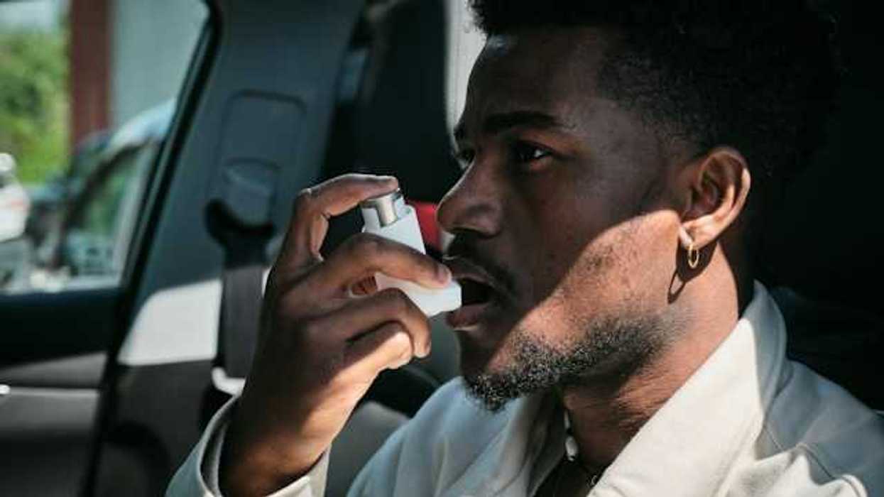 A Black man sitting in a car using an asthma inhaler