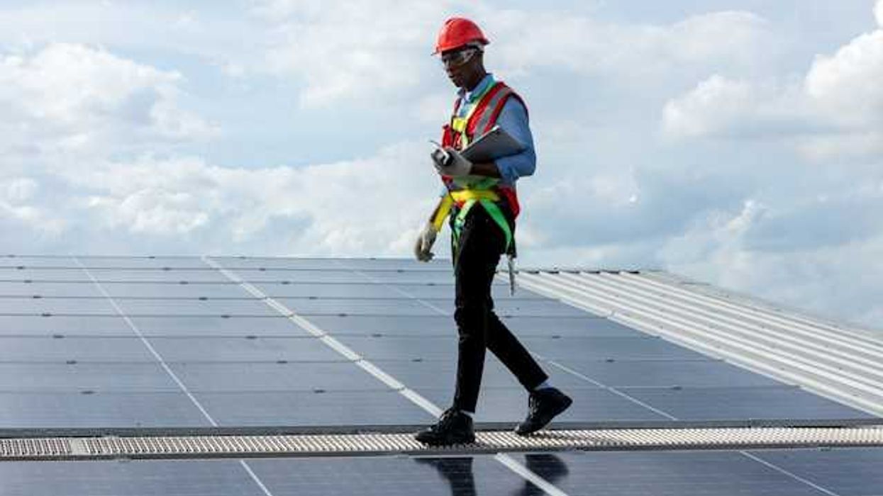 A black man walking on a solar panel installed on a roof
