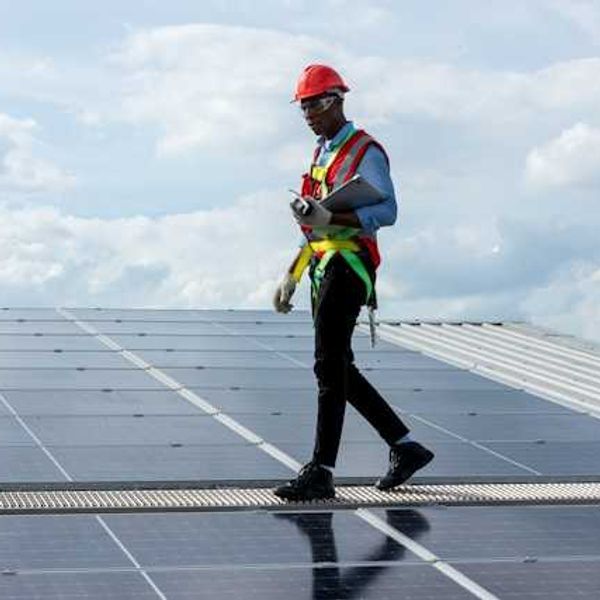 A black man walking on a solar panel installed on a roof