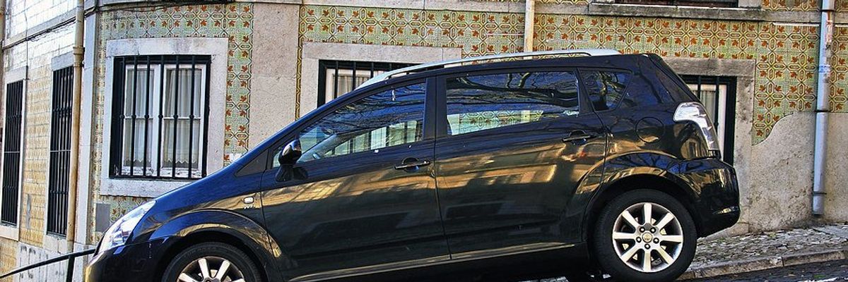 A black station wagon parked on a Lisbon street with a colorfully tiled house in the background.