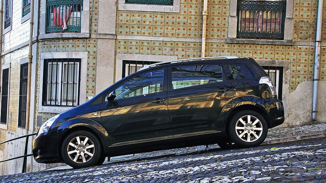 A black station wagon parked on a Lisbon street with a colorfully tiled house in the background.