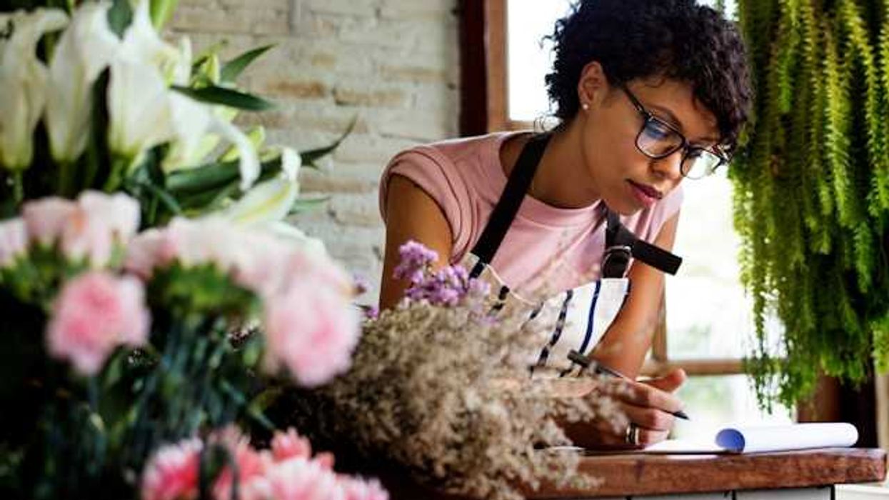 A Black woman leaning over a desk surrounded by flowers and greenery