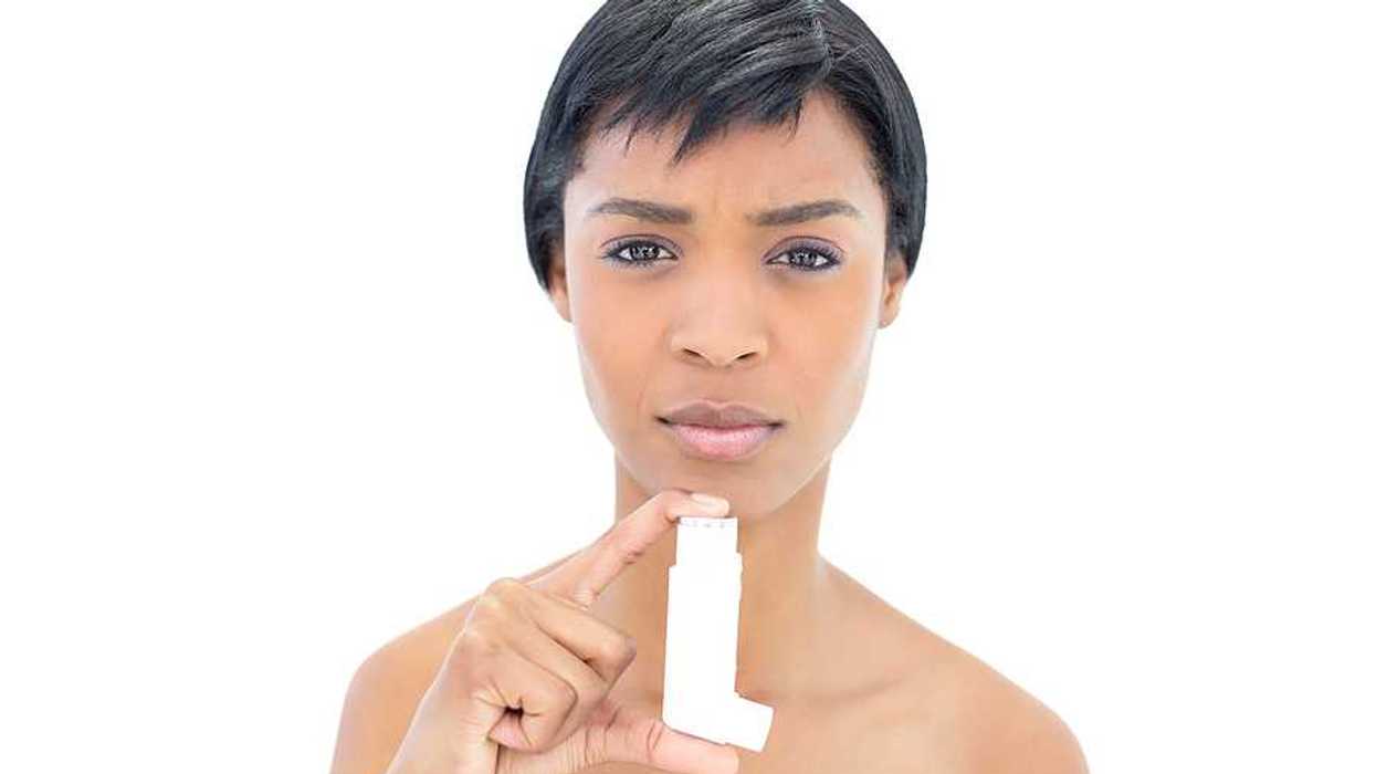A Black woman looking into the camera while holding an asthma inhaler