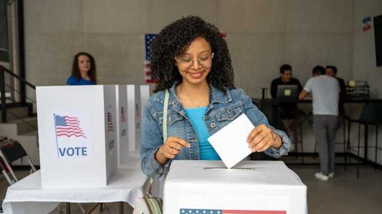 A Black woman putting her voting record into a box at a polling station