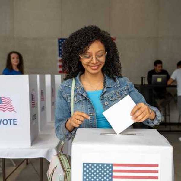 A Black woman putting her voting record into a box at a polling station