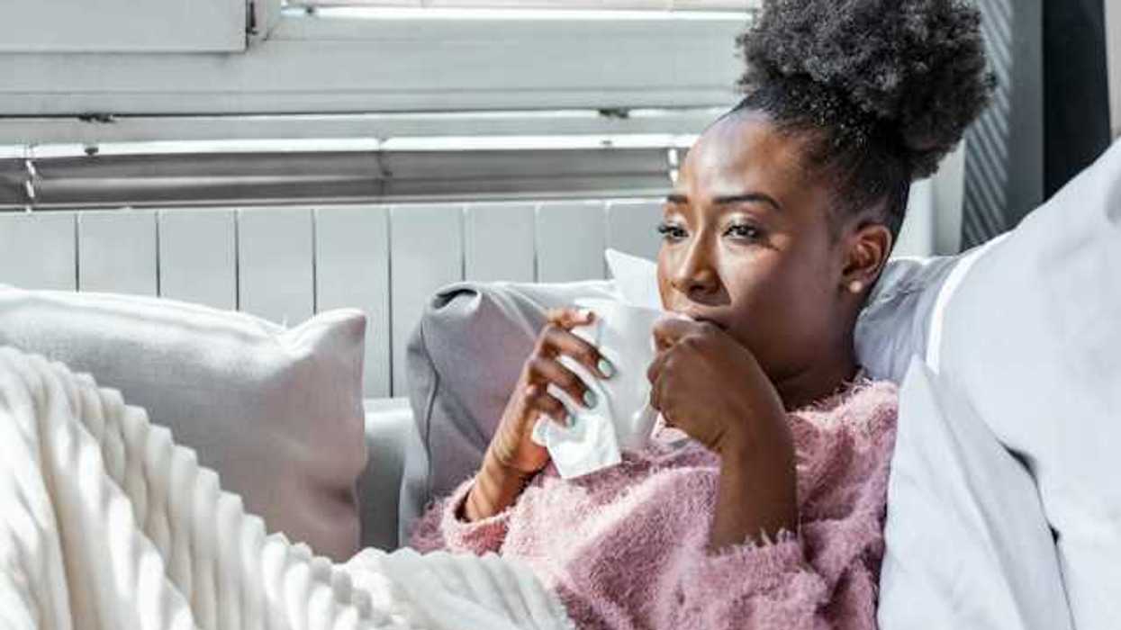 A Black woman sitting on a sofa drinking out of a white cup