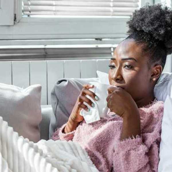 A Black woman sitting on a sofa drinking out of a white cup