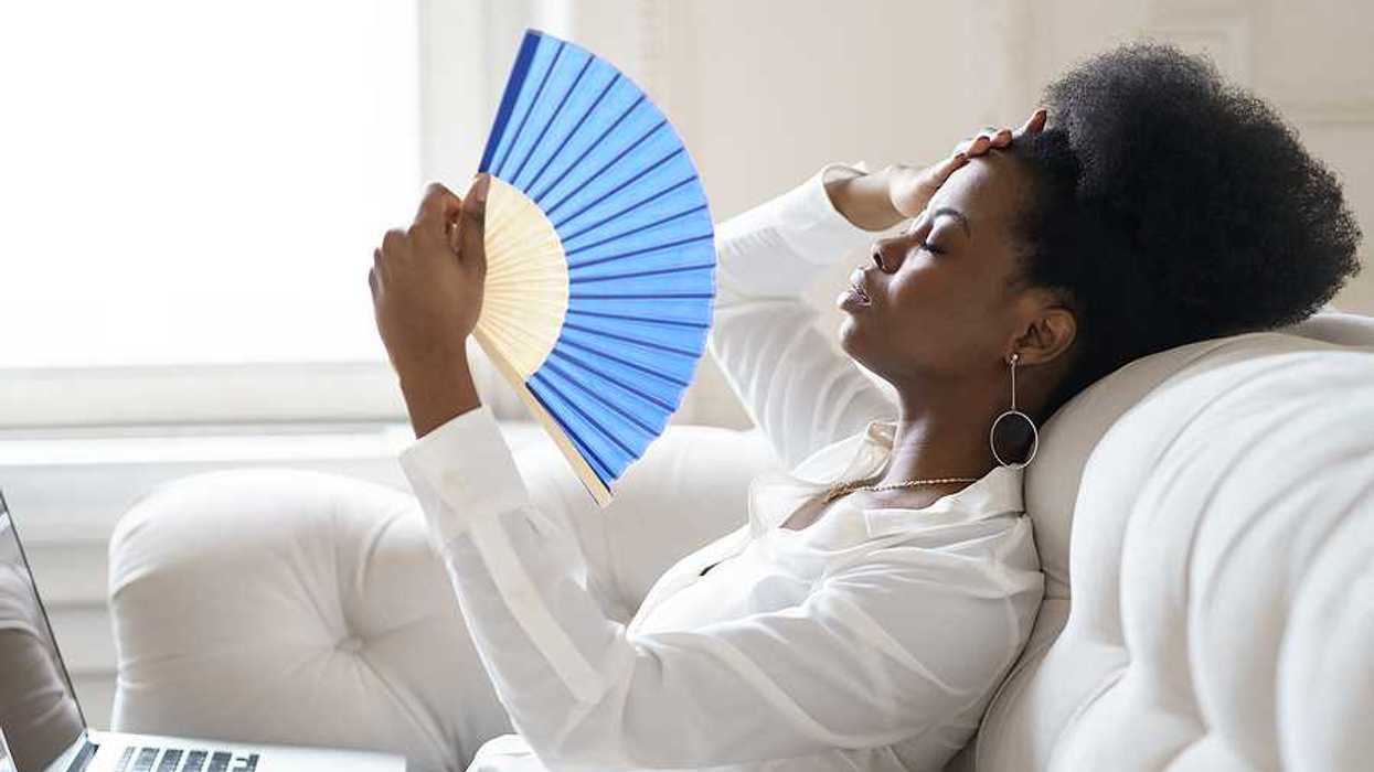 A Black woman sitting on a sofa with a blue hand fan