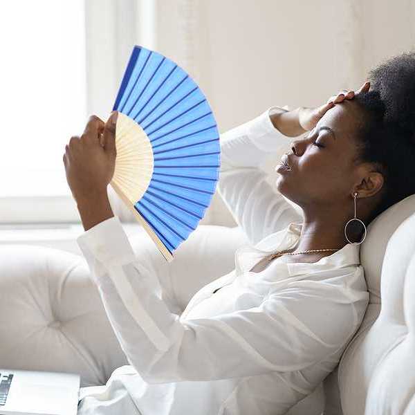 A black woman sitting on a sofa with a blue hand fan