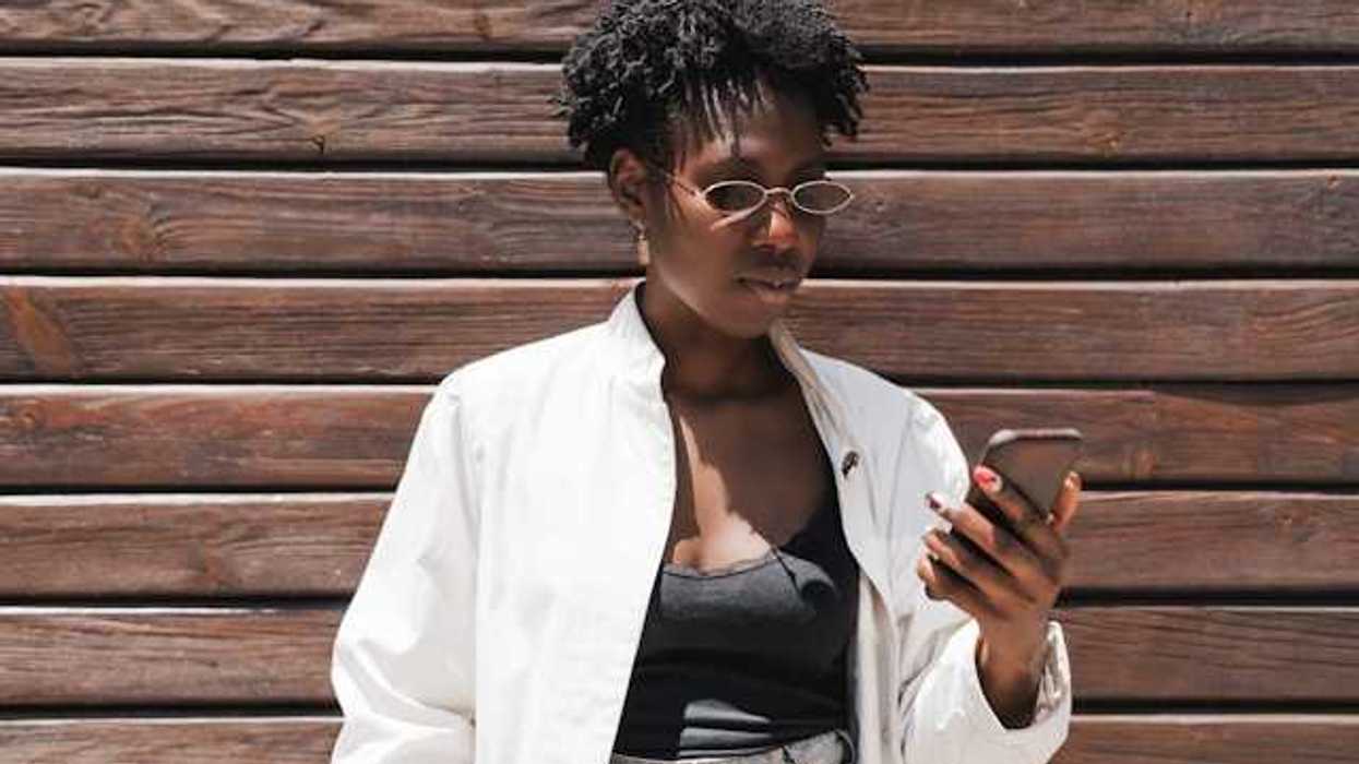 A Black woman standing against a wooden wall looking at her phone