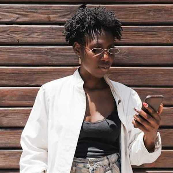 A Black woman standing against a wooden wall looking at her phone