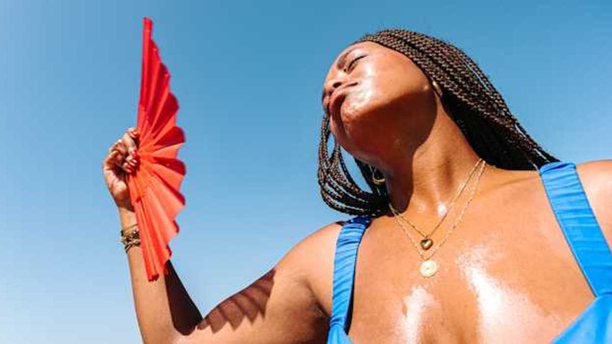 A Black woman using a red fan to cool her face on a hot day