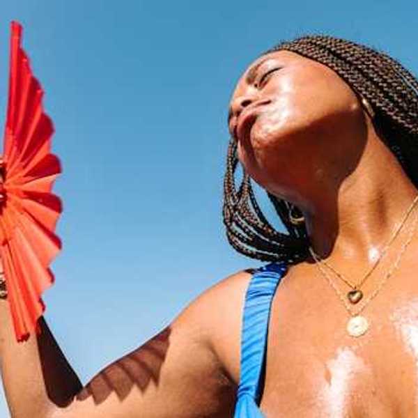 A Black woman using a red fan to cool her face on a hot day
