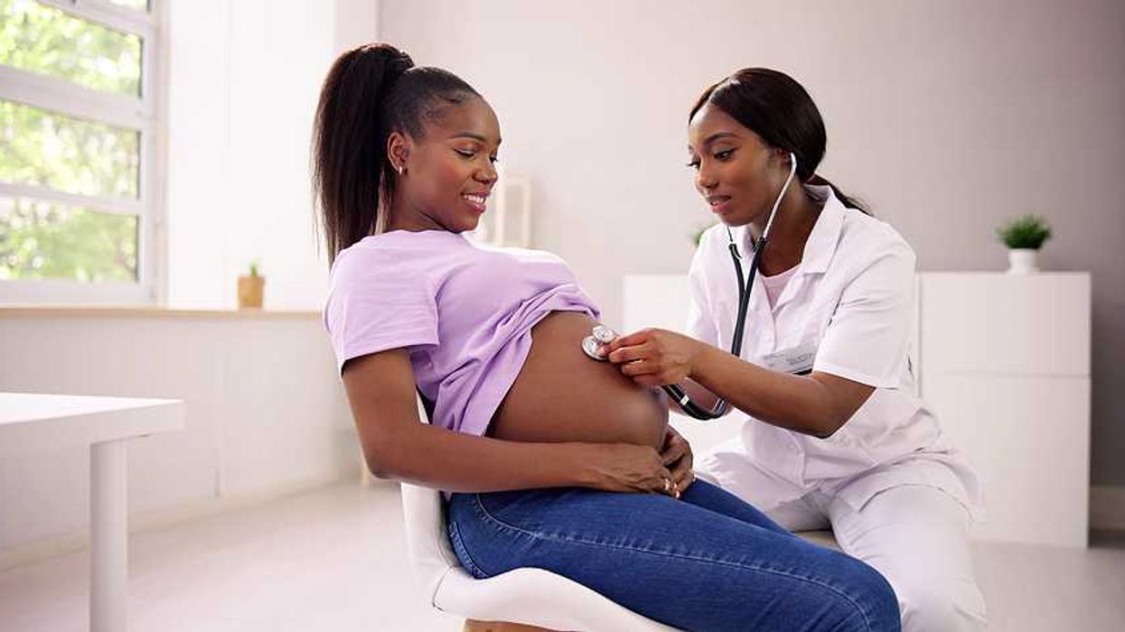 A Black woman with a stethoscope listening to the pregnant belly of another Black woman