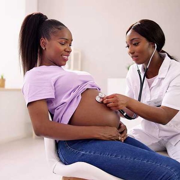 A Black woman with a stethoscope listening to the pregnant belly of another Black woman