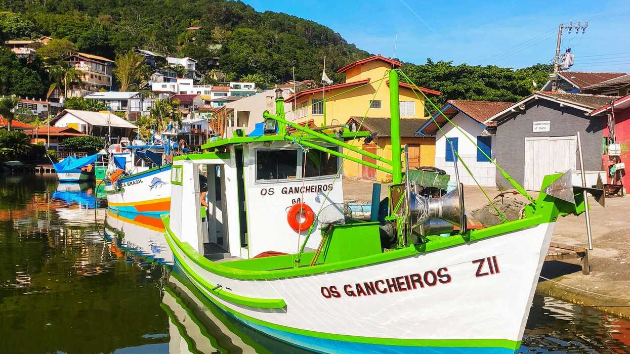 a boat is parked on the water with a village and green hillside in background.