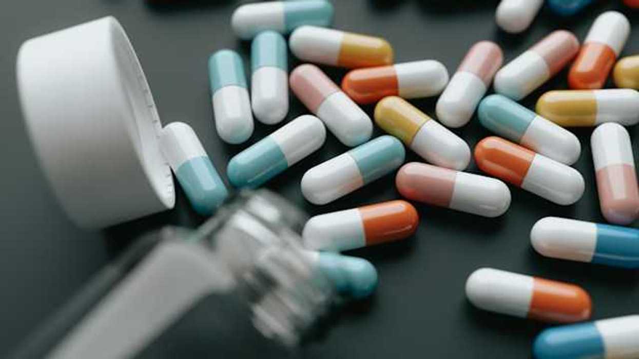 A bottle with multicolored pills spilling out onto a black surface
