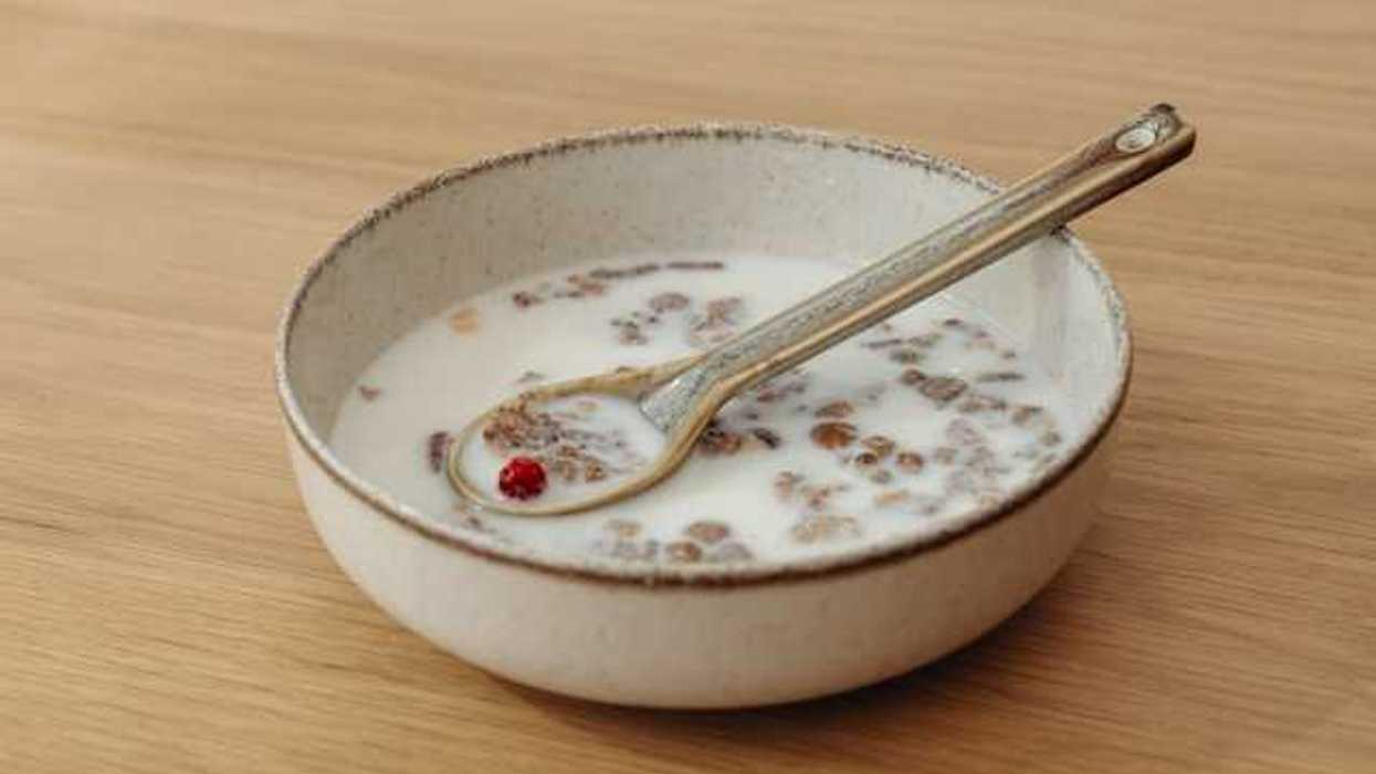 A bowl of cereal and milk with a silver spoon