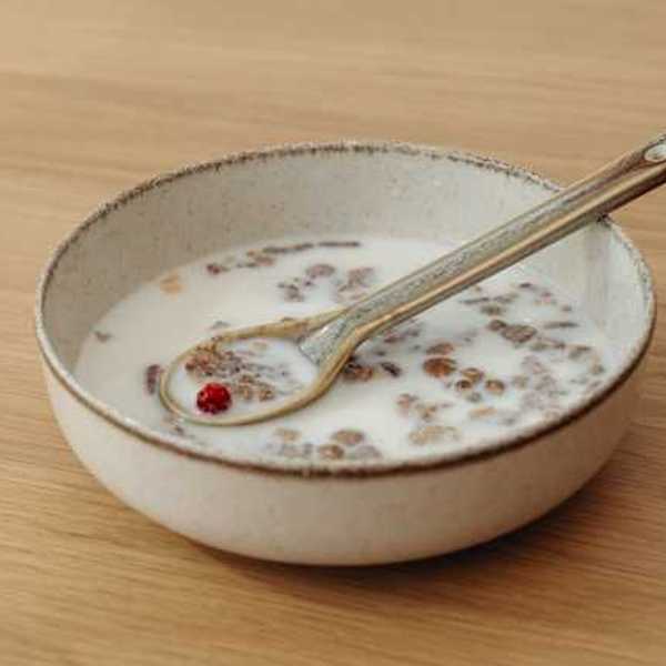 A bowl of cereal and milk with a silver spoon