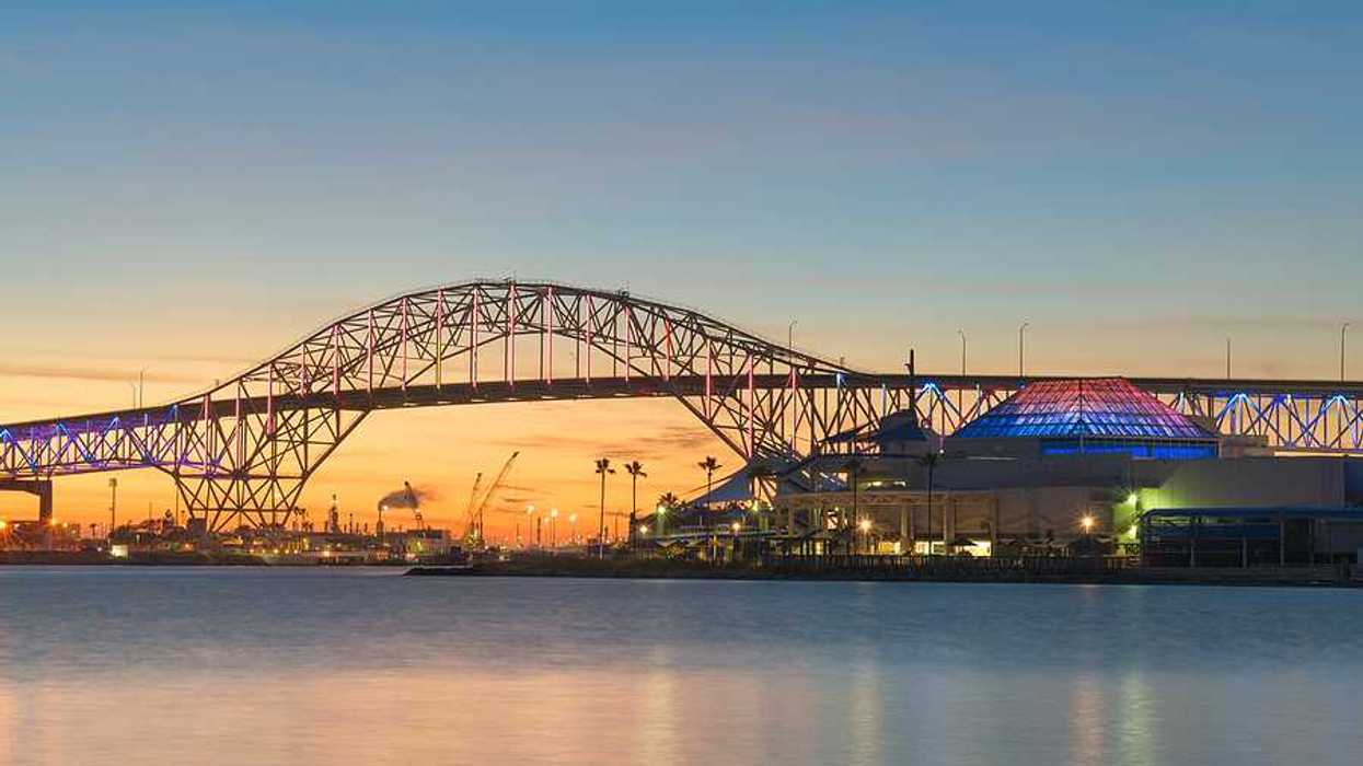 A bridge extending over a body of water with buildings and docks in the background at sunset