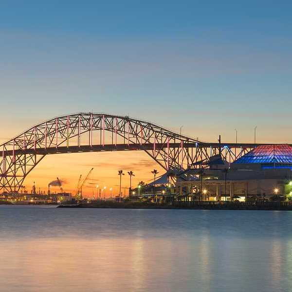A bridge extending over a body of water with buildings and docks in the background at sunset