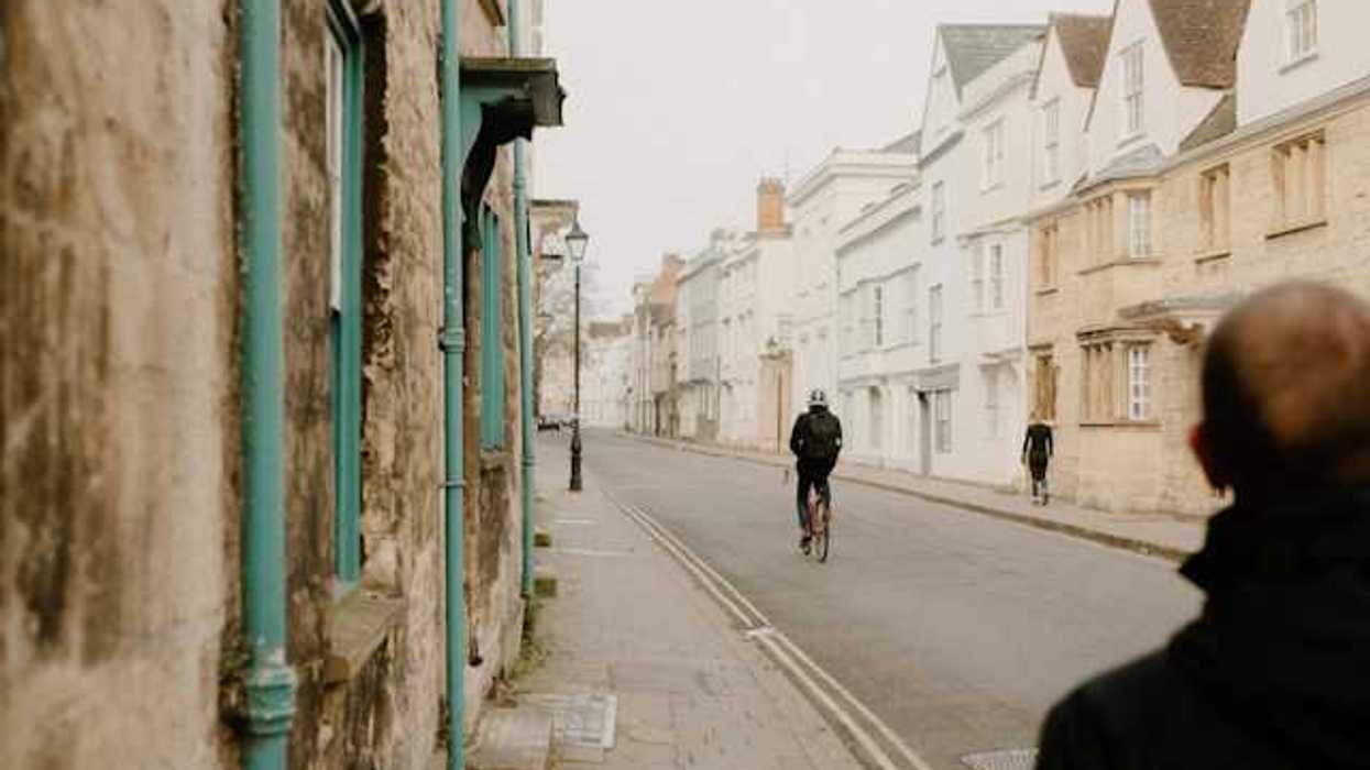 A British street on a cloudy day with a person on a bike and two pedestrians