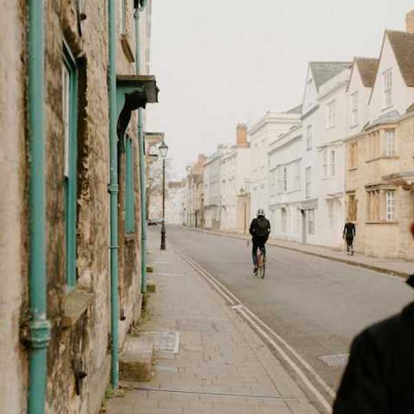 A British street on a cloudy day with a person on a bike and two pedestrians