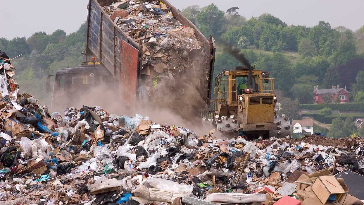 A bulldozer moving garbage on a landfill waste site as a garbage truck offloads more
