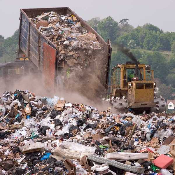 A bulldozer moving garbage on a landfill waste site as a garbage truck offloads more