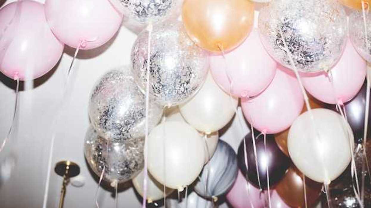 A bunch of pink, white and silver balloons hovering against a ceiling